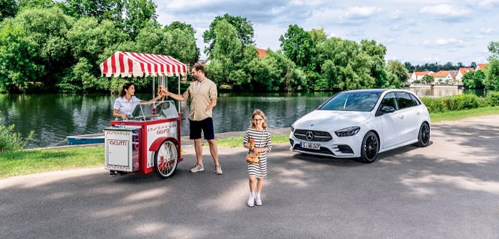 Vater und Tochter am Eisstand, Mercedes-Benz steht im Hintergrund